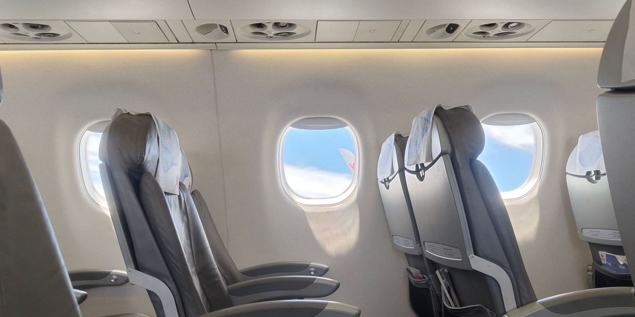 Empty airplane cabin with rows of passenger seats beside bright windows overlooking the clouds | Source: Pexels