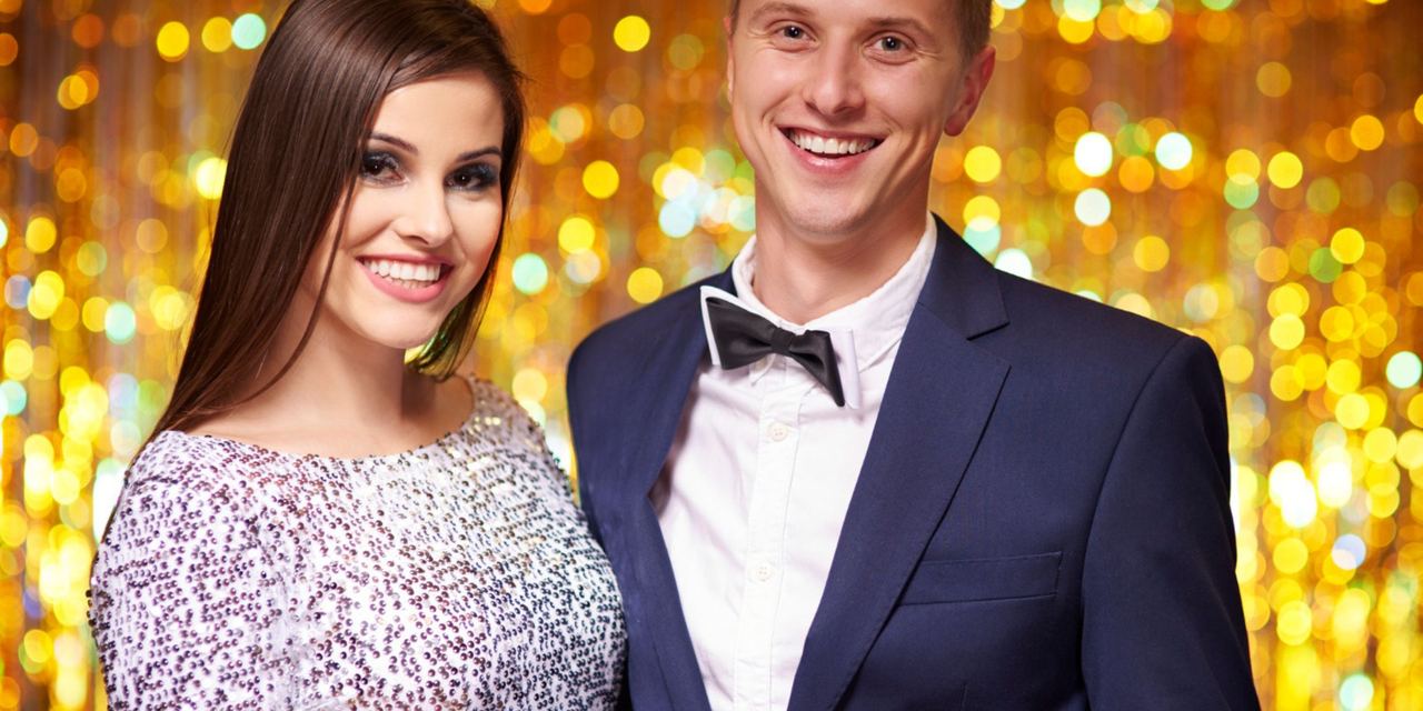A smiling young couple dressed in formal attire posing together against a backdrop of sparkling lights | Source: Magnific