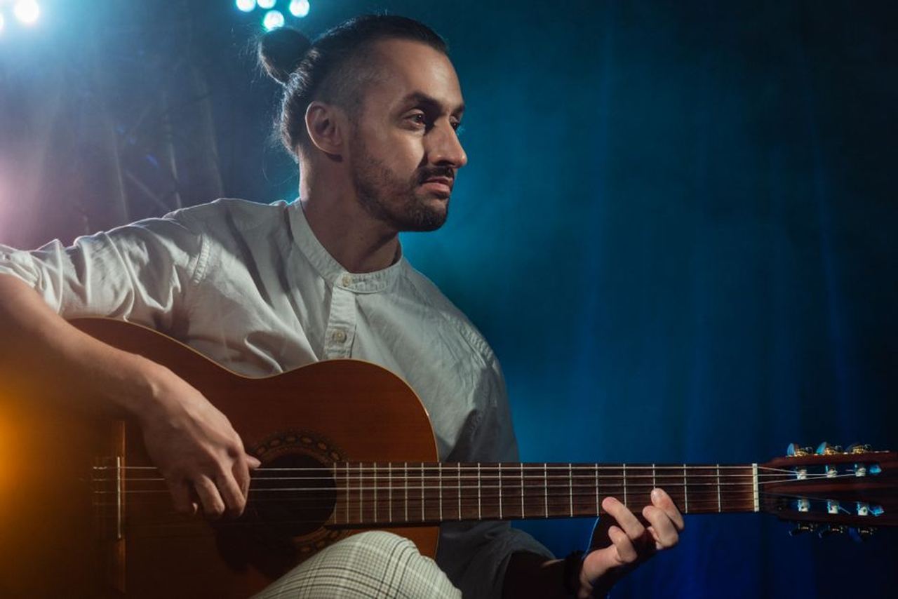 Caucasian male guitarist performing under stage lighting with acoustic guitar.