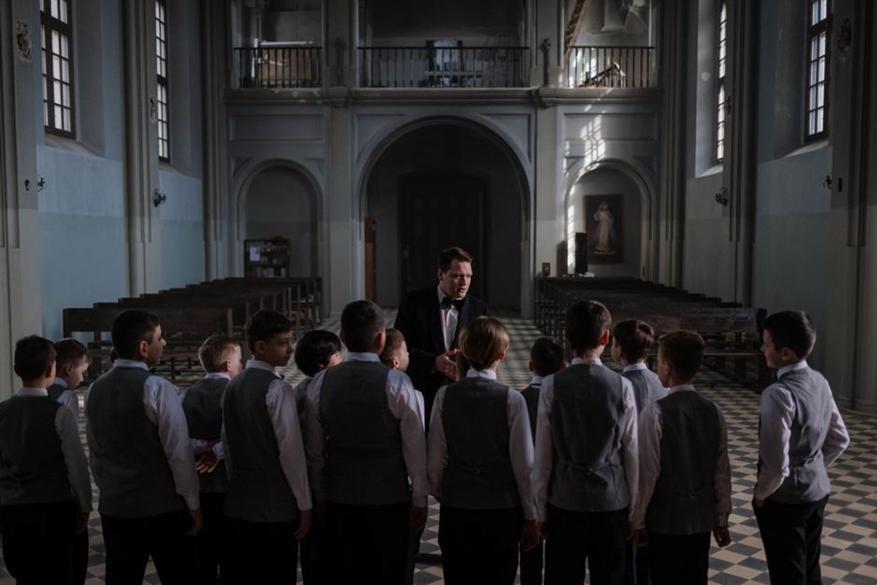 Boys choir rehearsing under conductor in an elegant cathedral setting.