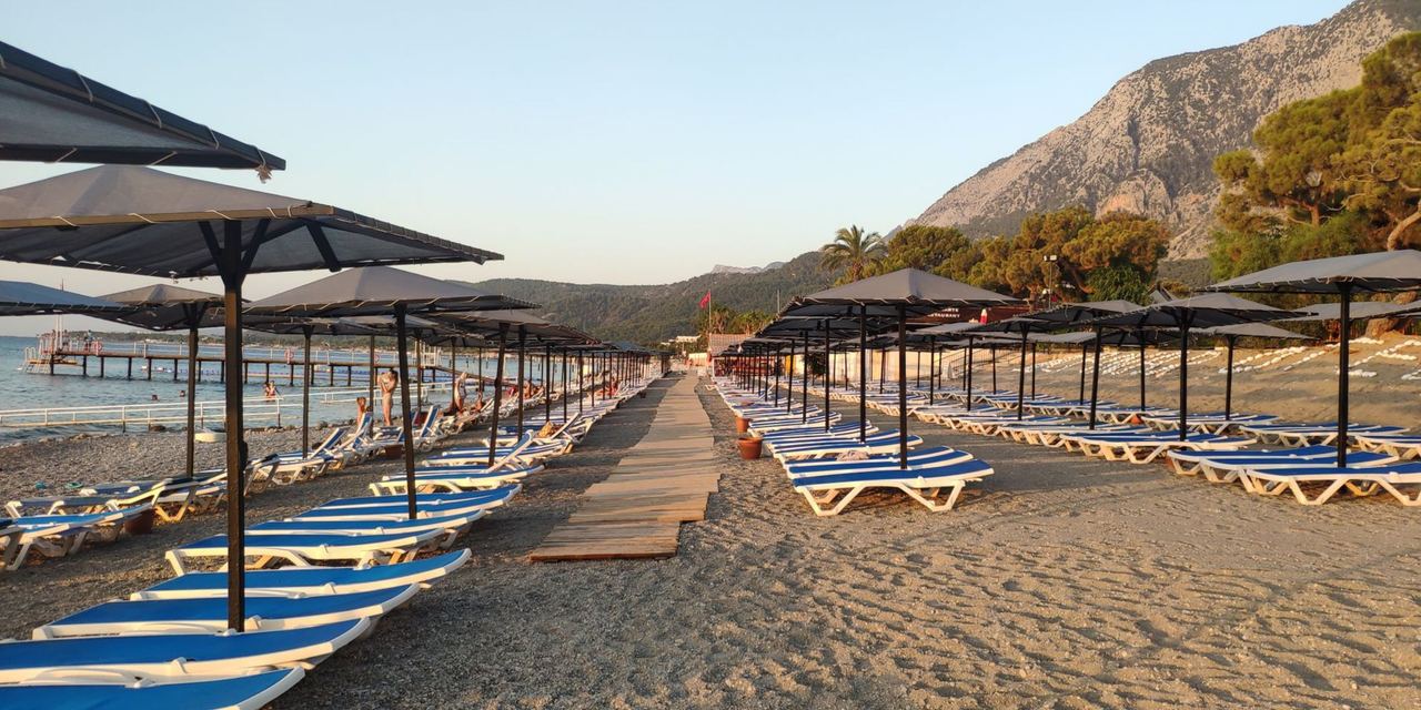 A quiet beach lined with rows of sun loungers and umbrellas, with mountains rising in the background | Source: Pexels