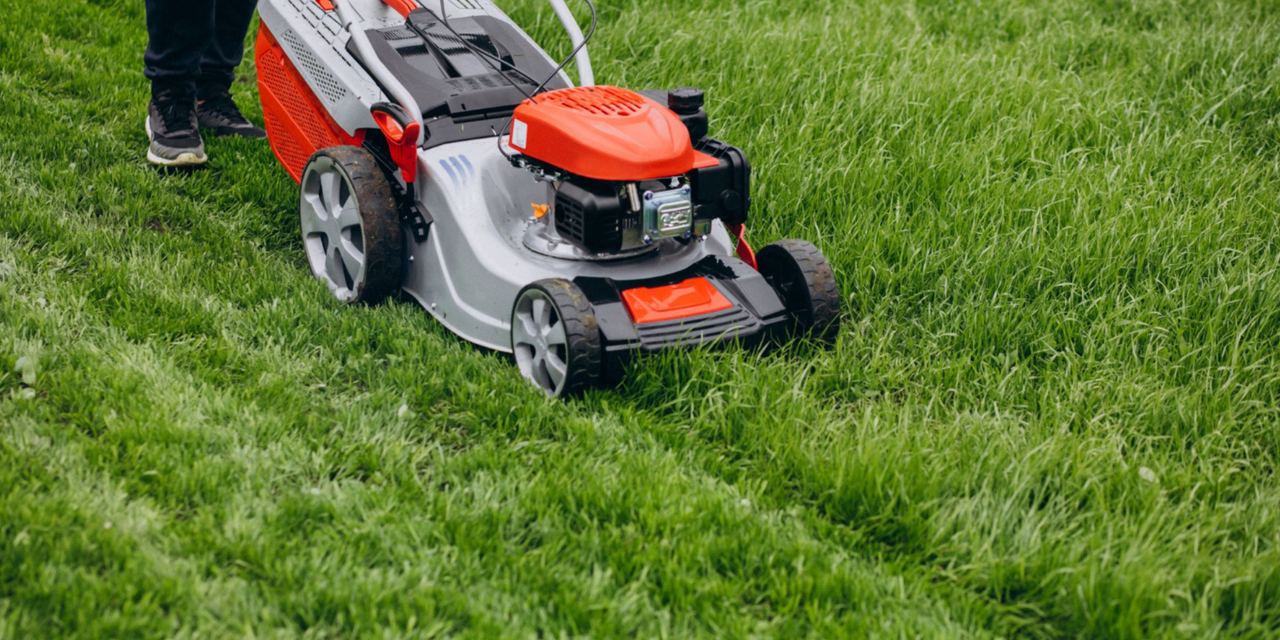 A person pushing a lawn mower across thick green grass | Source: Magnific