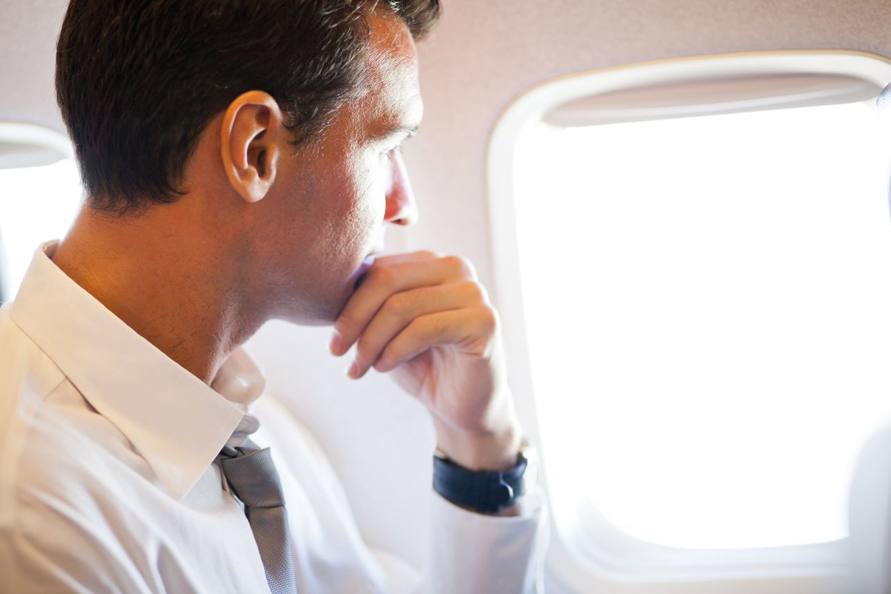 Thoughtful businessman on airplane looking outside | Source: Shutterstock