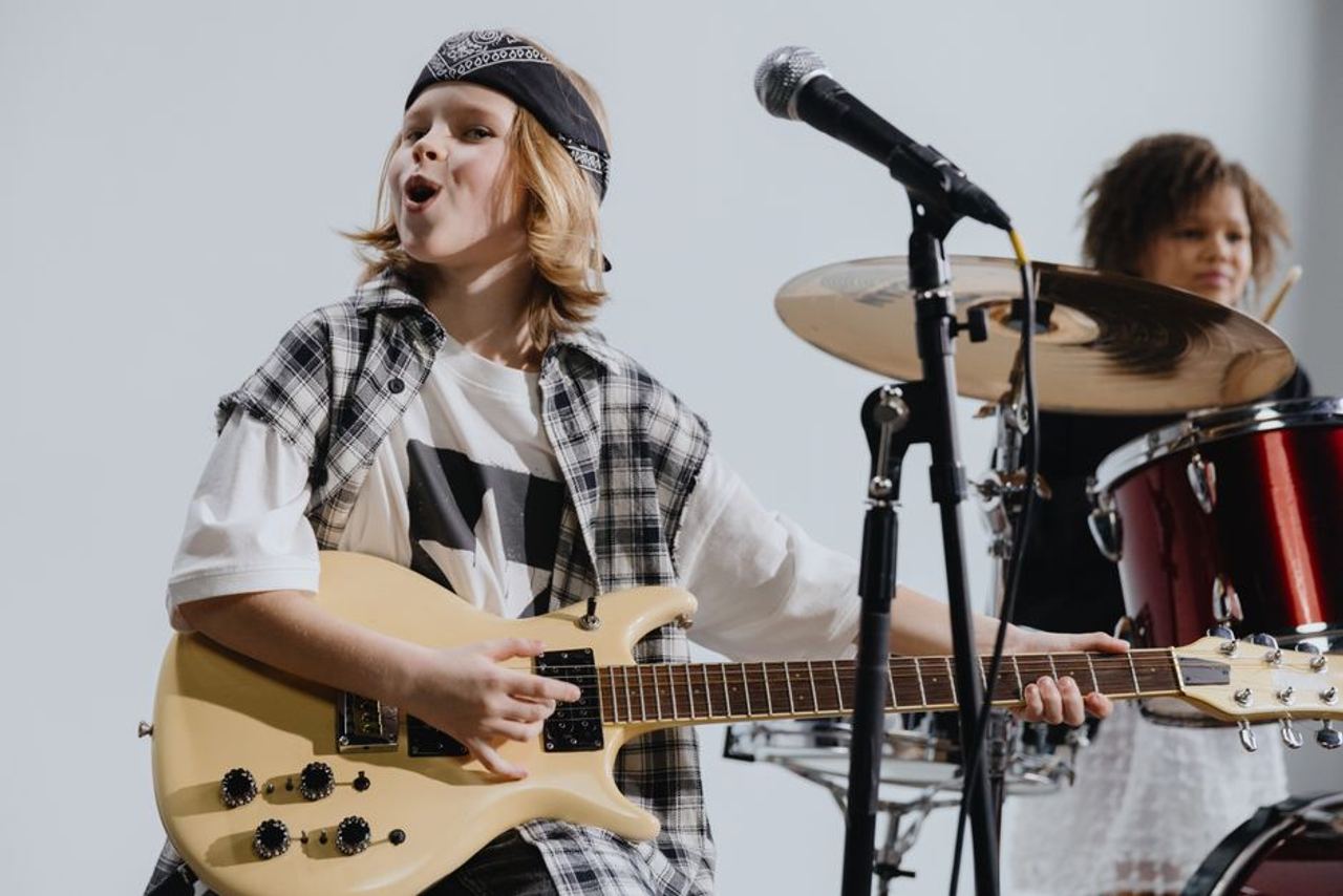 Young musicians passionately playing electric guitar and drums on stage, showcasing kids' musical talent.