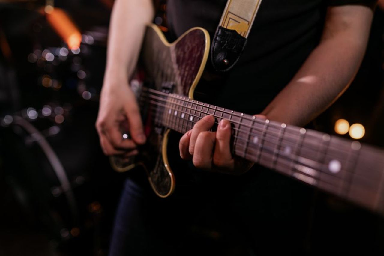 Musician strumming an electric guitar during live performance, emphasizing the strings and hands.