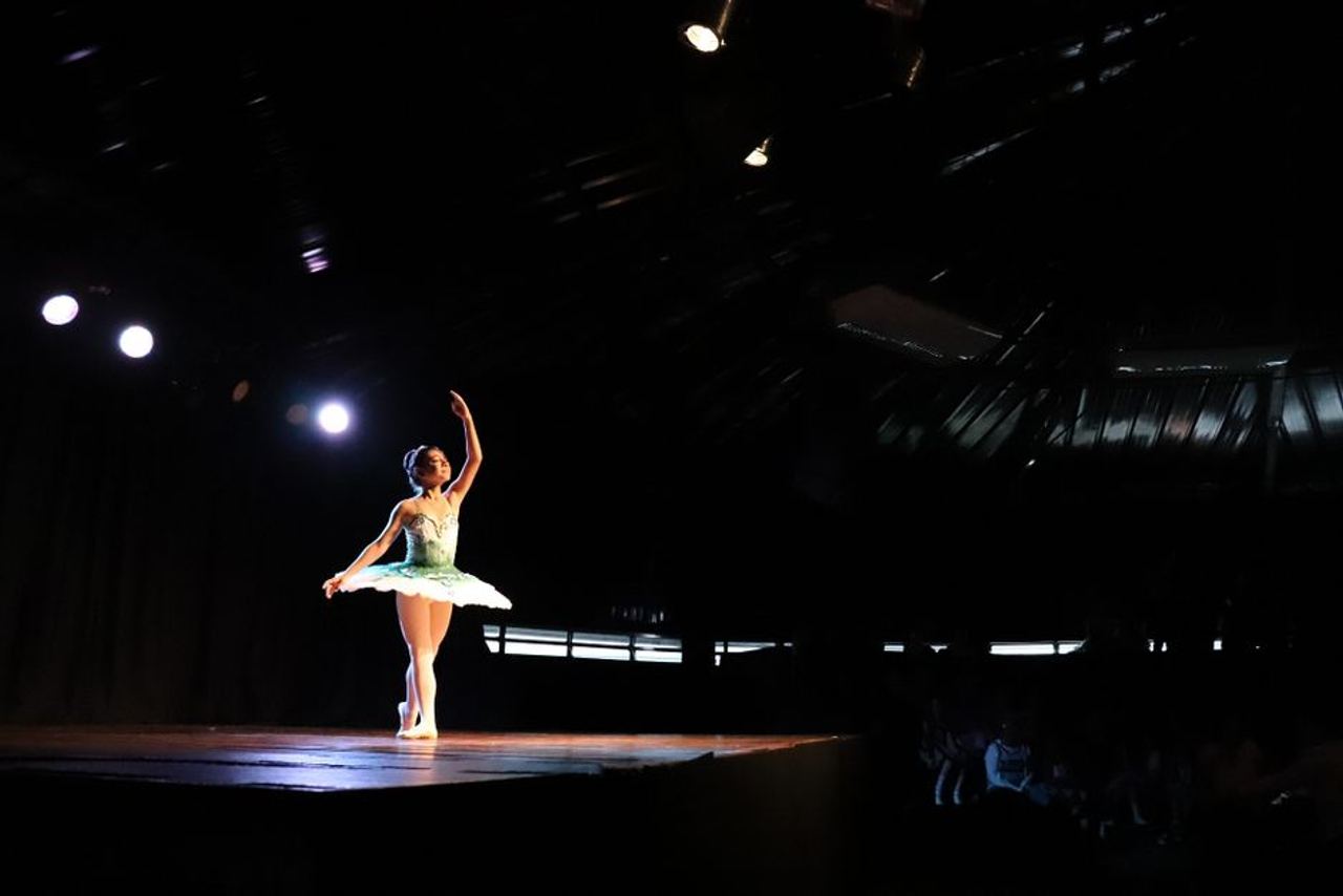 A graceful ballerina performing under spotlight in a theatre setting.