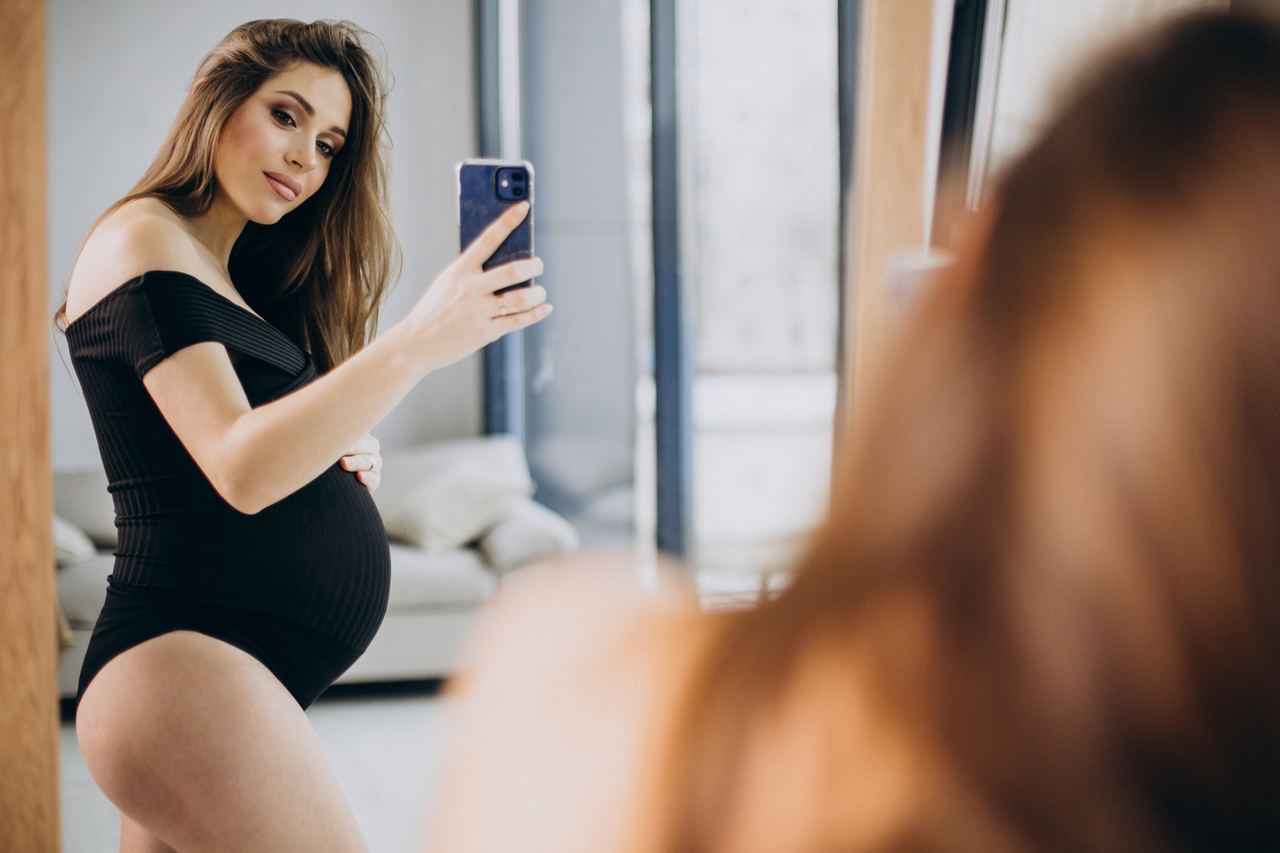 Pregnant woman holding her belly and looking into the mirror | Source: Magnific
