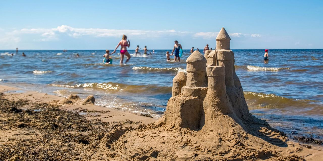 A sandcastle on the beach as families and children enjoy the shallow water on a sunny day | Source: Pexels