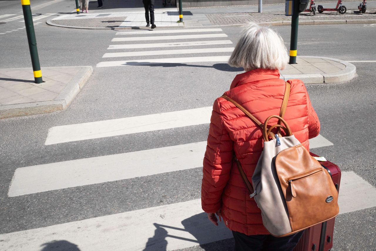An elderly woman in a red jacket with a backpack | Source: Pexels