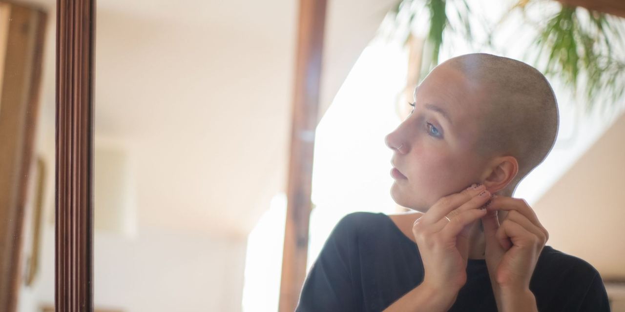 Woman with a shaved head looking into a mirror | Source: Pexels