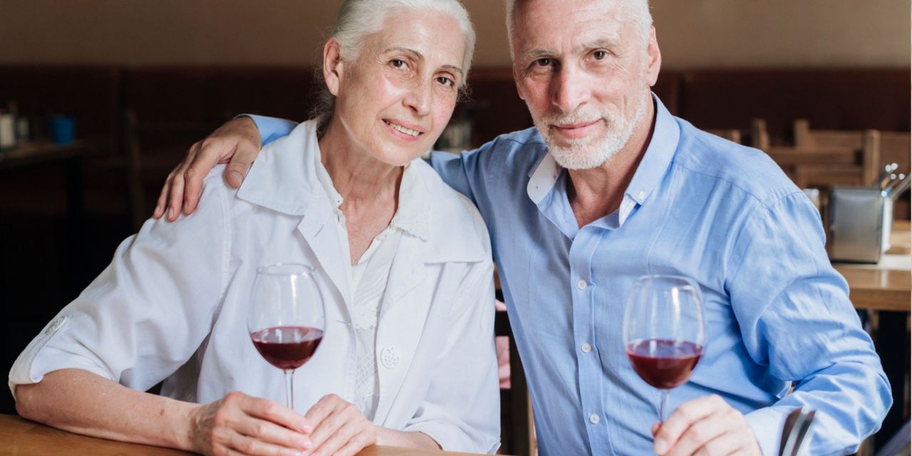A senior couple sitting together at a restaurant table, sharing a quiet moment over glasses of wine | Source: Magnific