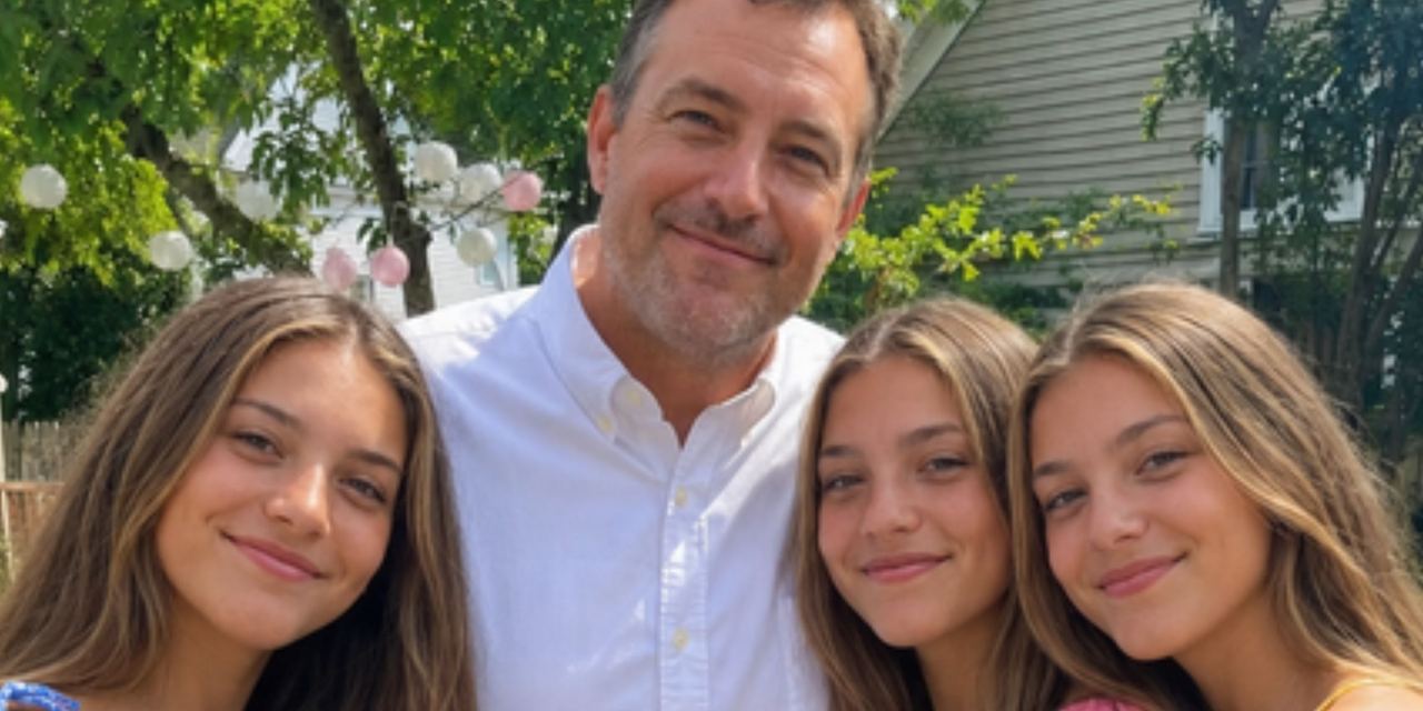 A smiling middle-aged father posing outdoors with his three daughters in a backyard | Source: AmoMedia