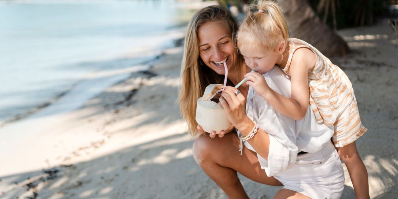 Mother and young daughter sharing a coconut drink on a tropical beach | Source: Magnific