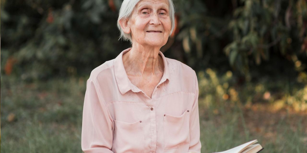 Elderly woman sitting outdoors with a book | Source: Magnific