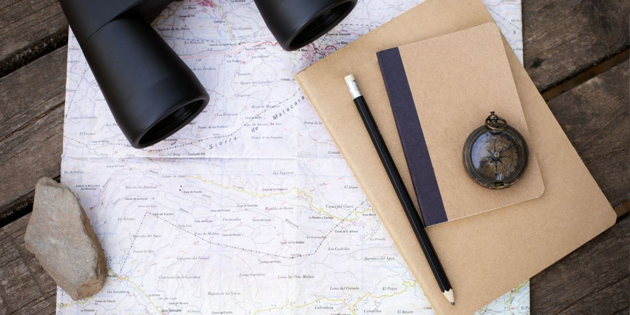 A map, notebook, and compass arranged beside binoculars | Source: Magnific