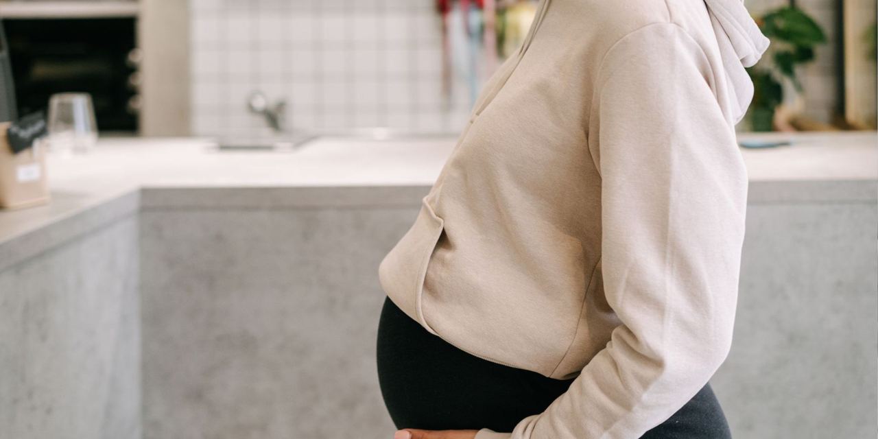 A pregnant woman gently cradling her baby bump while standing in a cozy home kitchen | Source: Pexels