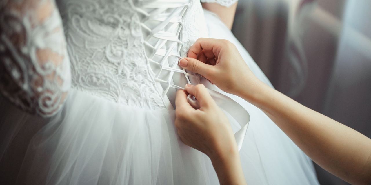 A person lacing up the back of a bride's wedding dress while helping her get ready for the ceremony | Source: Magnific