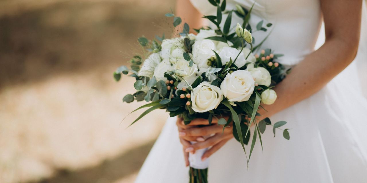 A bride in a white wedding dress holding an elegant bouquet of white roses | Source: Magnific