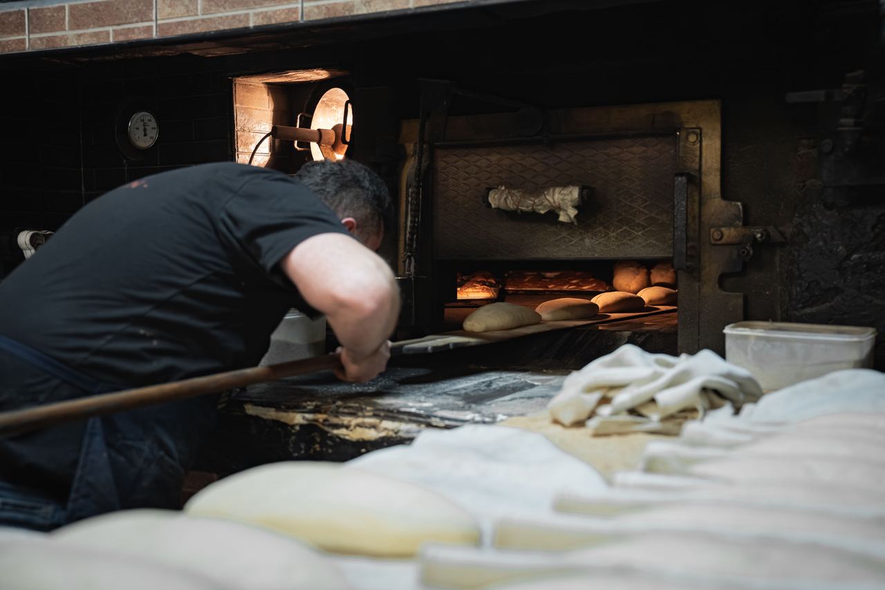 A baker places loaves in a rustic wood-fired oven | Source: Pexels