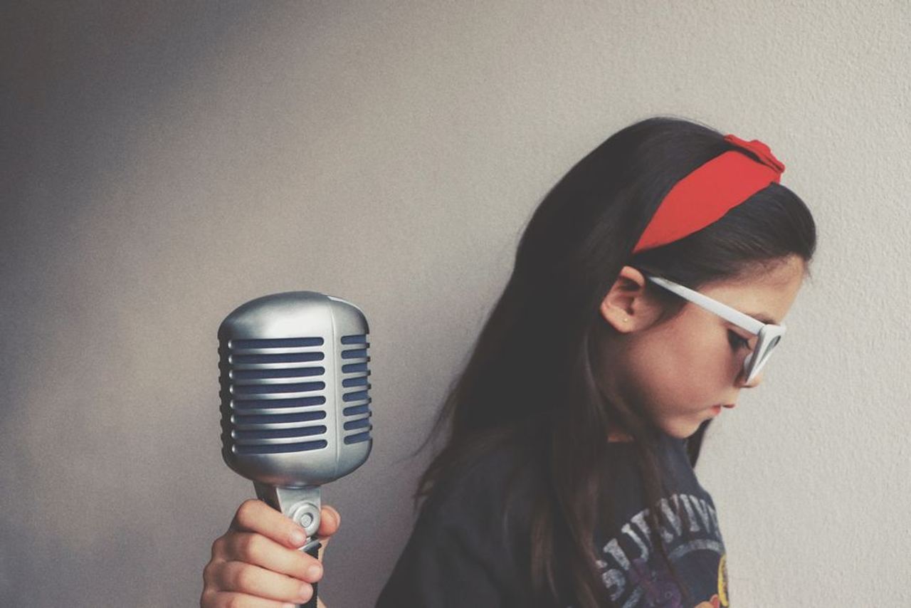 Child wearing a red headband and sunglasses, holding a vintage microphone.