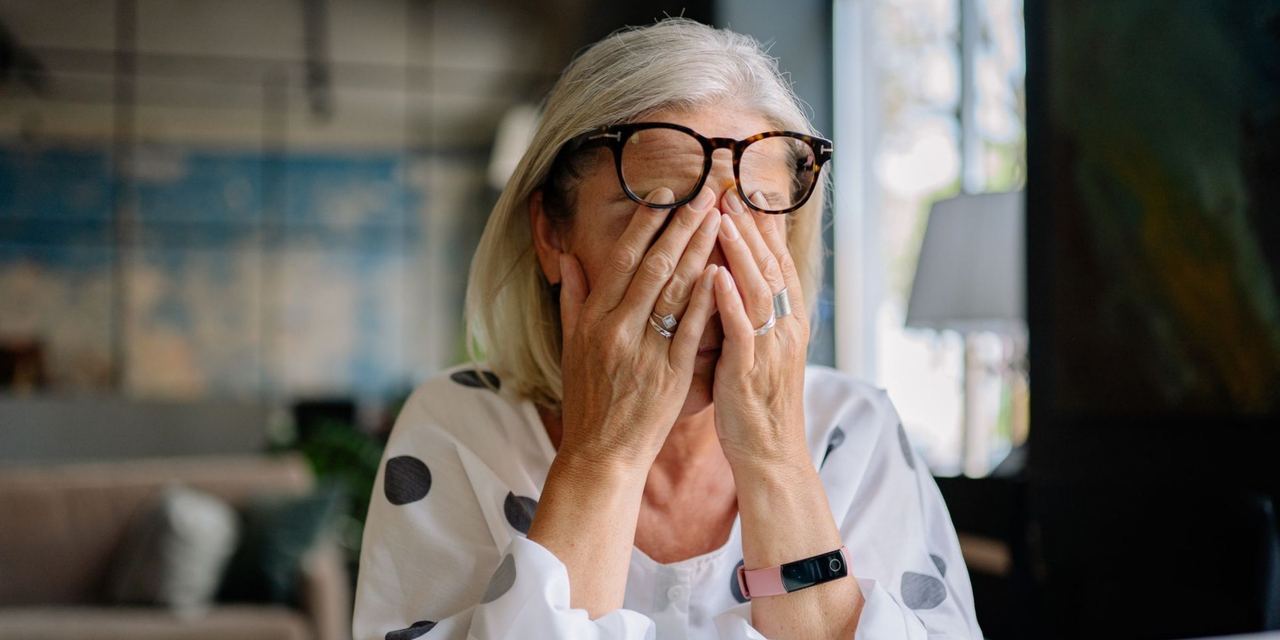 An elderly woman is stressed indoors, covering her face with her hands | Source: Pexels