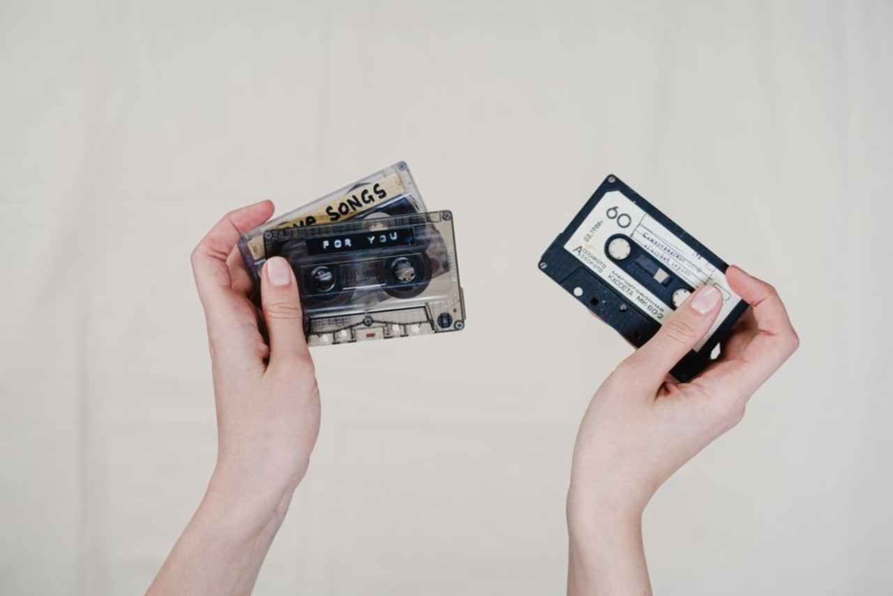 Two hands holding retro cassette tapes with handwritten labels, nostalgic music format.