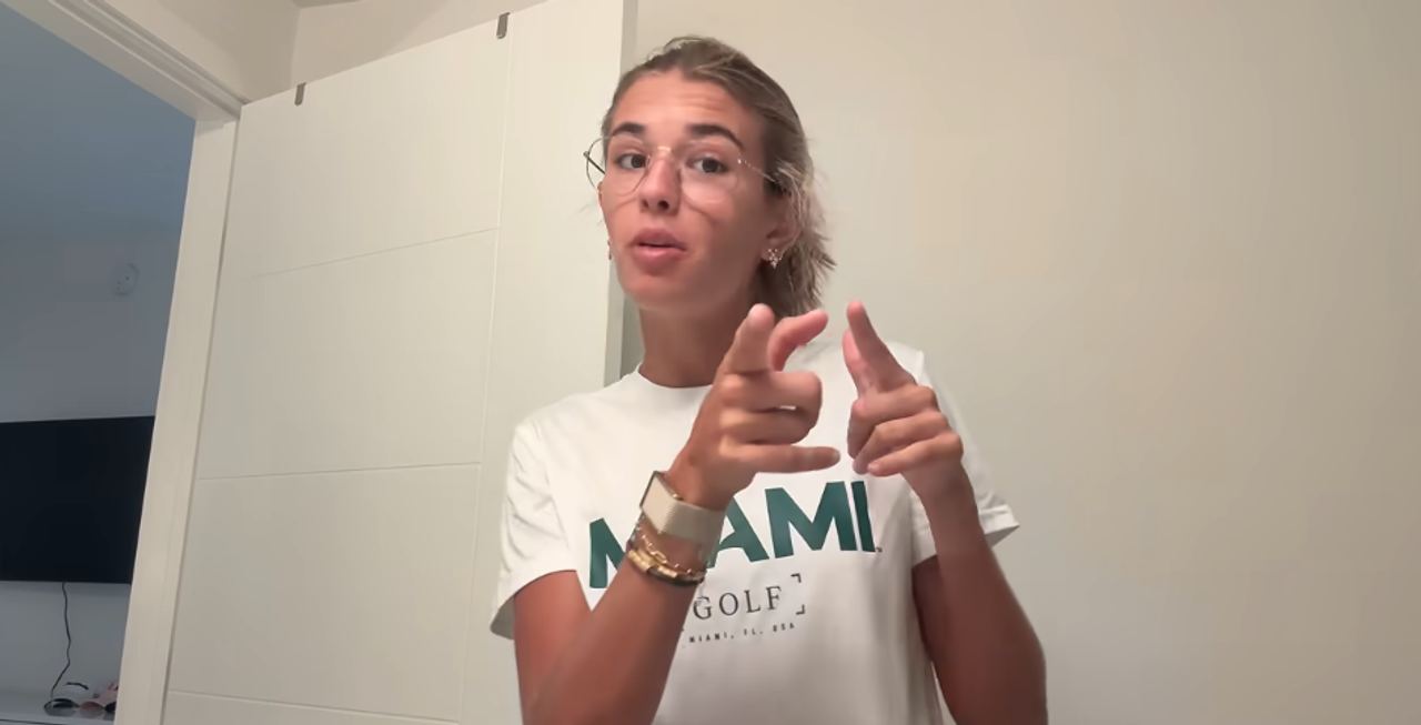 Nineteen-year-old Kai Trump kicked off her apartment tour by sharing her morning routine in a video posted on September 5, 2026. Wearing round wire-rimmed glasses and a white University of Miami golf t-shirt, she spoke directly to the camera against a plain white interior door. | Source: YouTube/Kai Trump