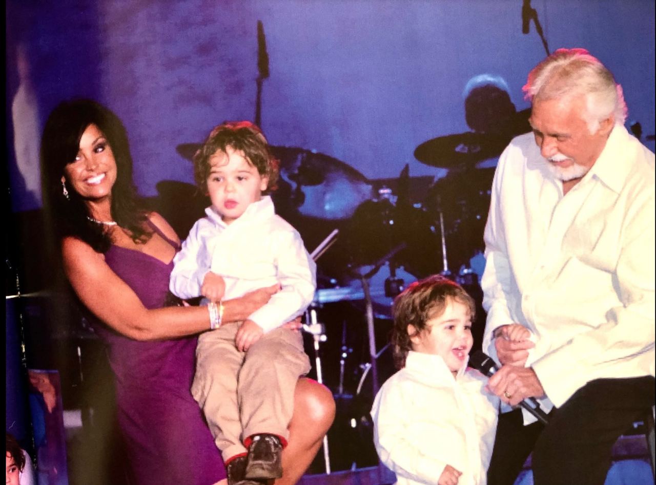 The early family photo shows Kenny Rogers and Wanda Miller sharing the stage with their young twin sons, Justin and Jordan, offering a glimpse of the boys years before their grown-up appearance sparked a lively debate over who they resemble. | Source: Facebook/Kenny Rogers