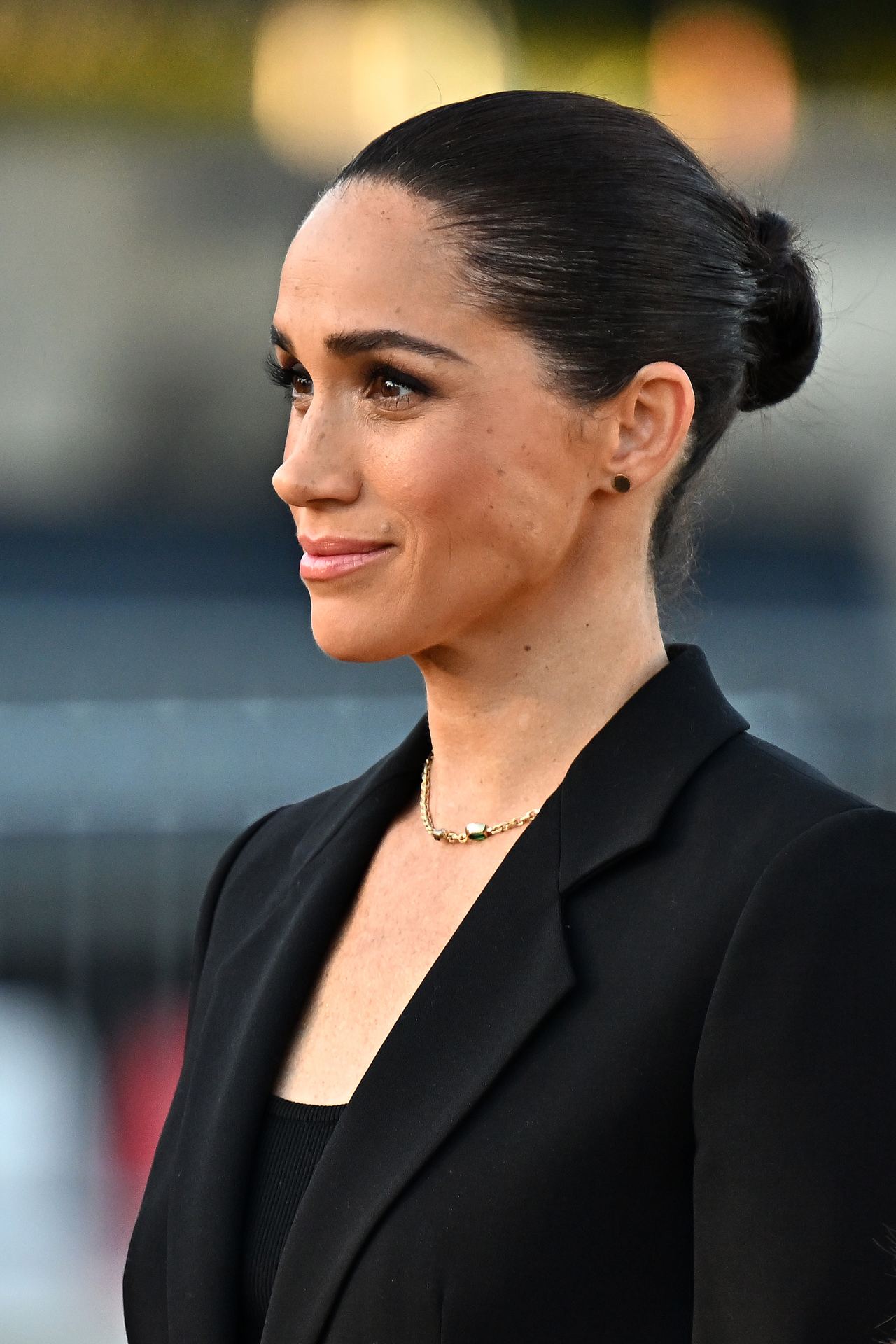 Meghan Markle attends an event in a black tailored ensemble, wearing her hair in a sleek bun and accessorizing with a gold necklace and stud earrings. | Source: Getty Images
