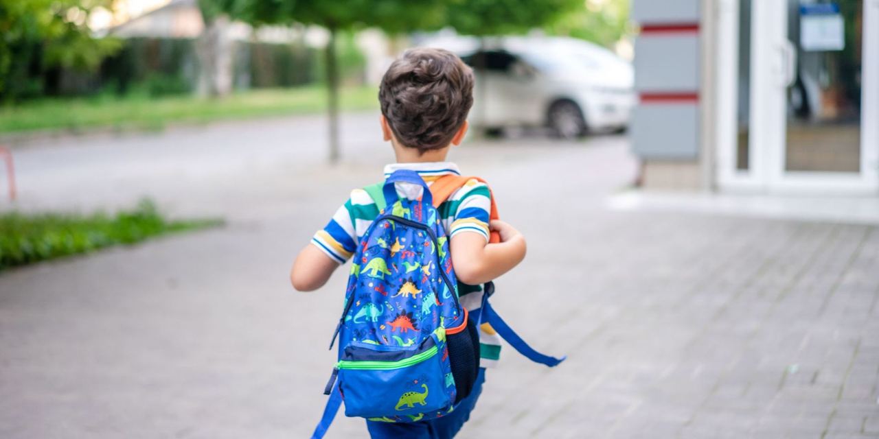 Young boy wearing a backpack walking toward a school building | Source: Pexels