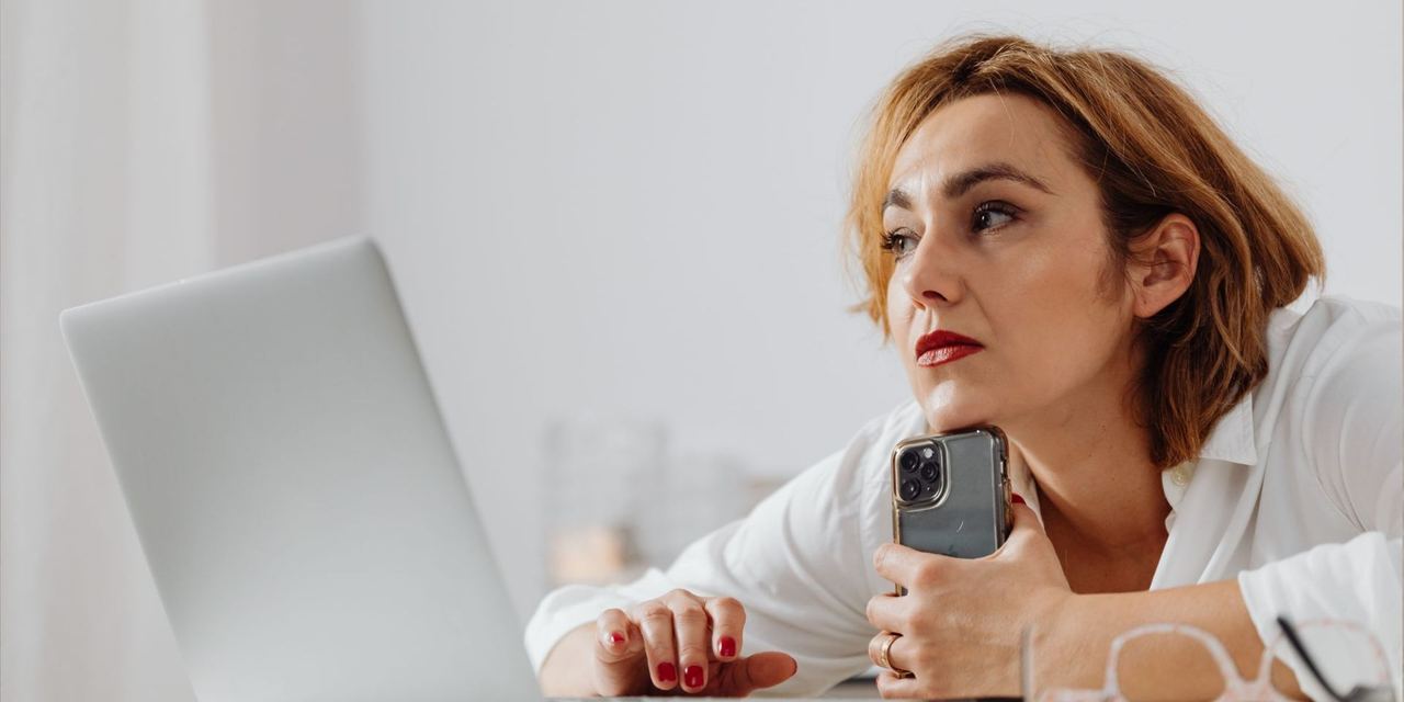A sad woman holding her phone while using a laptop | Source: Pexels