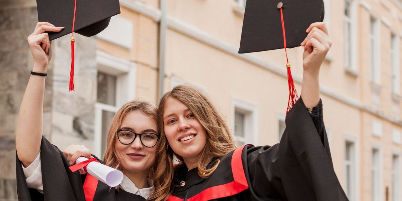 Two graduates in caps and gowns celebrating their achievement while holding up their graduation caps and diploma | Source: Magnific