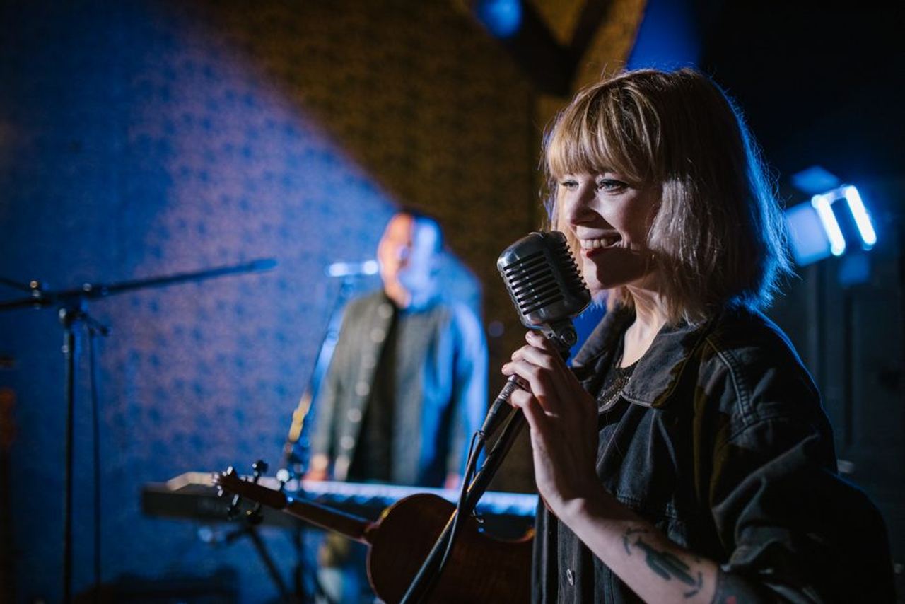Smiling caucasian woman singing with vintage microphone during live music performance.