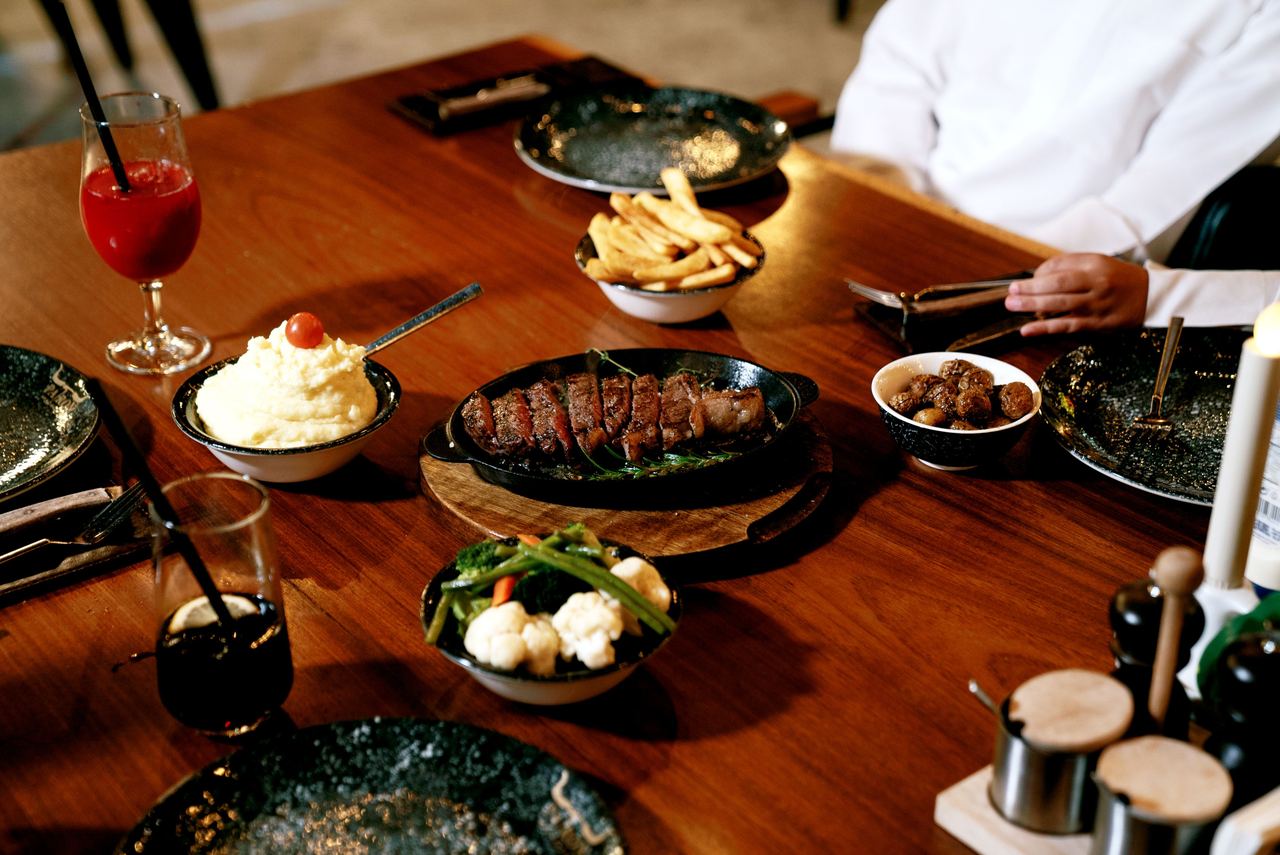Delicious gourmet dish featuring steak, French fries, and vegetables, served on a wooden table indoors | Source: Pexels
