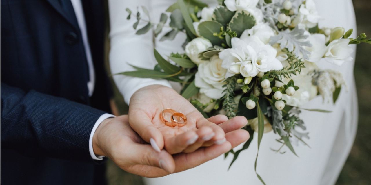 Couple holding wedding rings with a bridal bouquet | Source: Magnific