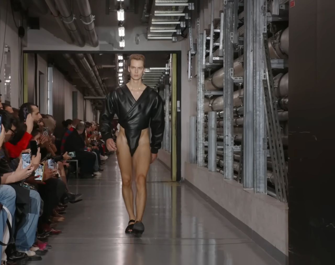 Then came futuristic bodysuits cut high on the leg. This model wears a black version with a voluminous, inflated design that highlights his toned legs — a distinctive take on the bodysuit, tailored to the male physique. From a post dated October 5, 2025. Source: Youtube/@jeanpaulgaultier