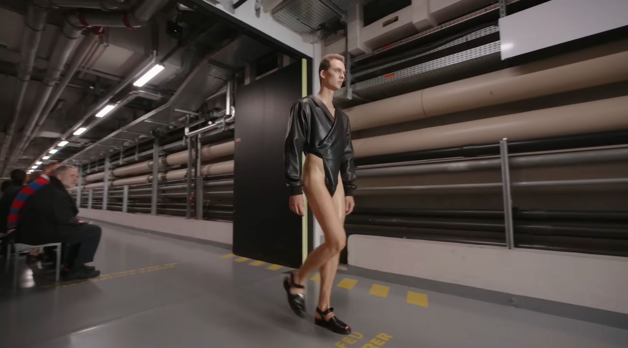 The model rounds the corner, revealing just how high the bodysuit’s cuts go. He pairs the look with black open shoes, adding to the futuristic vibe — a glimpse of what daring fashion might look like in the years ahead. From a post dated October 5, 2025. Source: Youtube/@jeanpaulgaultier