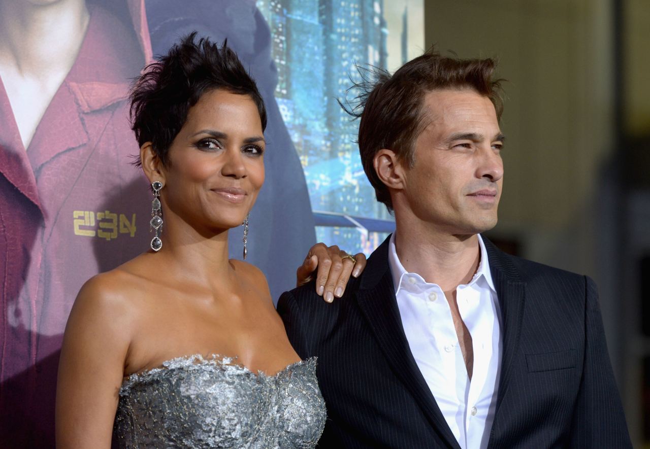 Actors Halle Berry and Olivier Martinez posed for cameras at the Warner Bros. Pictures' "Cloud Atlas" premiere at Grauman's Chinese Theatre on October 24, 2012, in Hollywood, California. Berry dazzled in a strapless silver-grey textured lace dress, accessorized with ornate dangling earrings and her trademark edgy pixie cut, while resting a hand on the shoulder of Martinez, who looked sharp in a dark pinstripe suit jacket paired with an open-collar white shirt. | Source: Getty Images