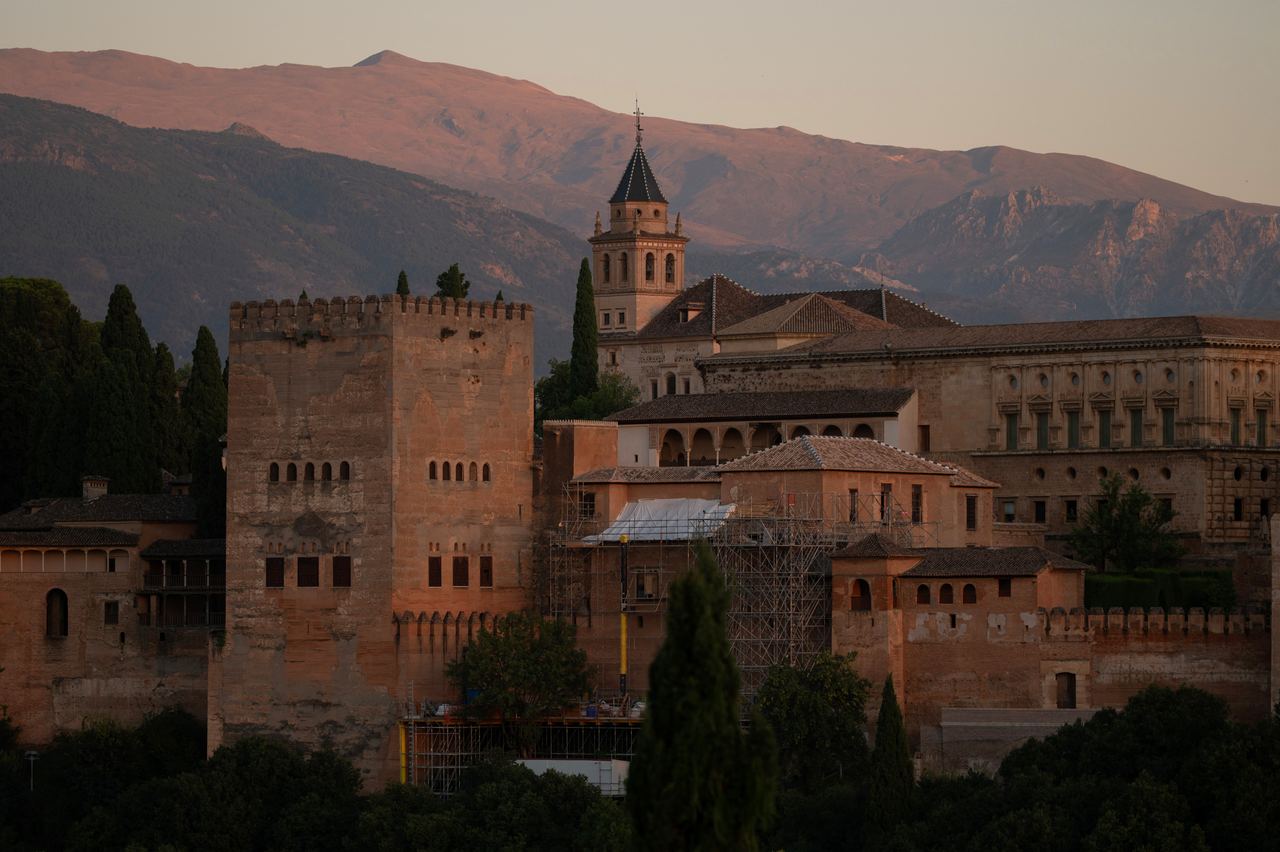 A scenic view captured the historic fortress and towers of the Alhambra from Saint Nicholas square following an earthquake in Granada on August 18, 2026. The ancient reddish stone architecture, church tower, and ongoing restoration scaffolding stood bathed in warm twilight against the towering backdrop of the Sierra Nevada mountains. | Source: Getty Images