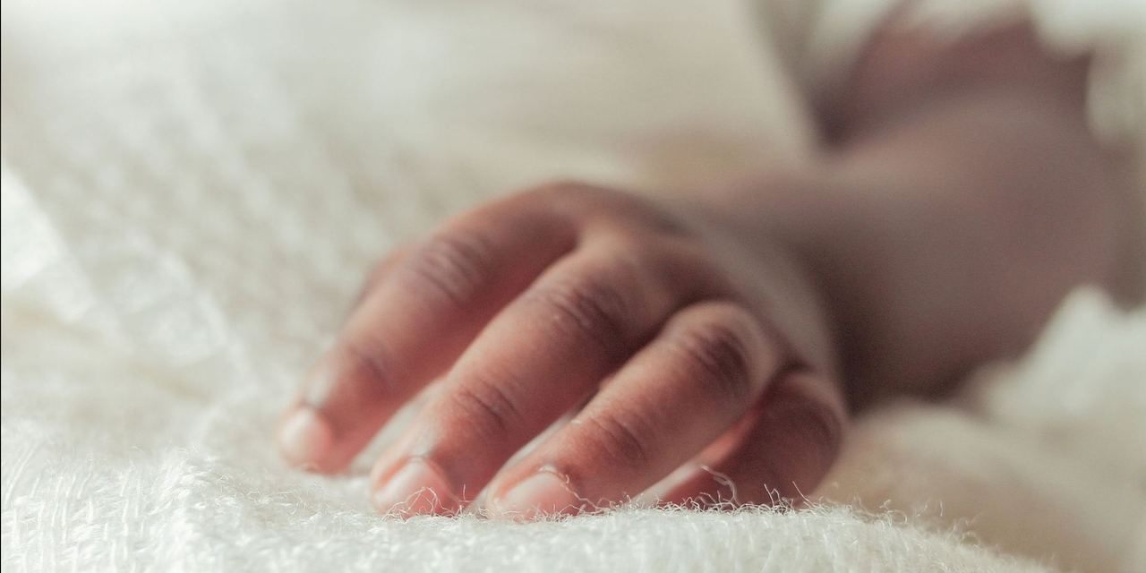 A close-up of a boy's hand gently resting on soft white fabric | Source: Pexels