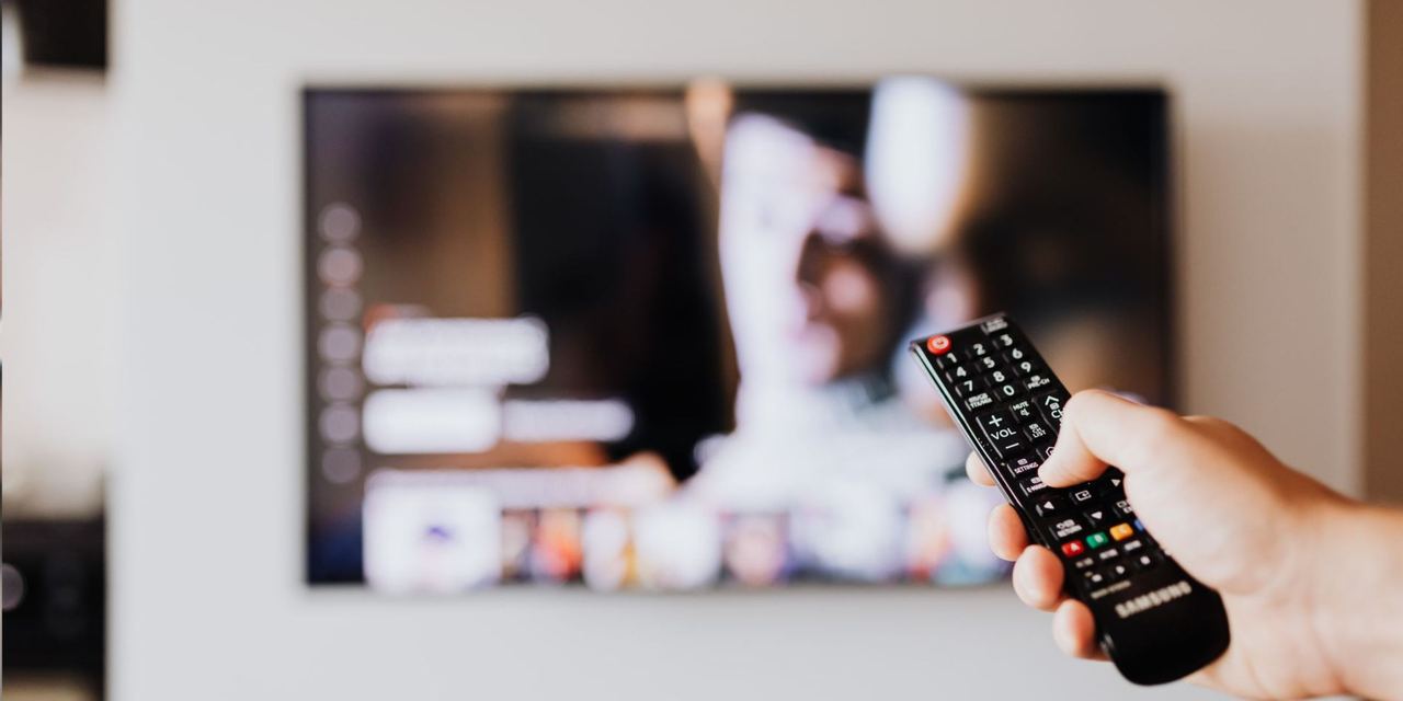 A person using a TV remote control with a blurred TV screen in the background | Source: Pexels