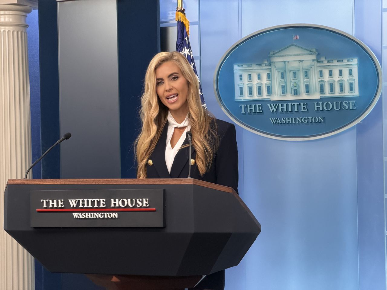 White House Press Secretary Katie Zacharia speaks at the podium during a news briefing in the James S. Brady Press Briefing Room at the White House on October 13, 2026, in Washington, D.C. Delivering remarks before the official White House emblem, she wears a navy-blue double-breasted blazer adorned with gold buttons over a high-neck white blouse with a delicate collar tie, her long blonde hair styled in loose waves over her shoulders. | Source: Getty Images