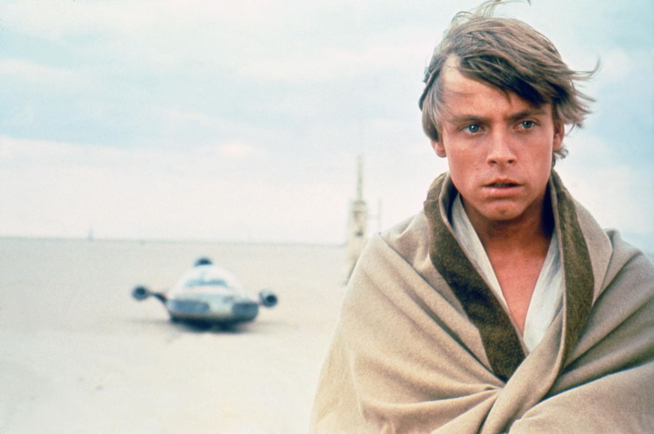 The actor stood against the stark desert landscape during production of "Star Wars: A New Hope," with the character's landspeeder visible in the distance. Wrapped in light-colored clothing beneath the open sky, he embodied the young hero before audiences knew his name. The production still provided another clear view of his appearance before the January 1977 accident that resulted in reconstructive treatment for his facial injuries. | Source: Getty Images