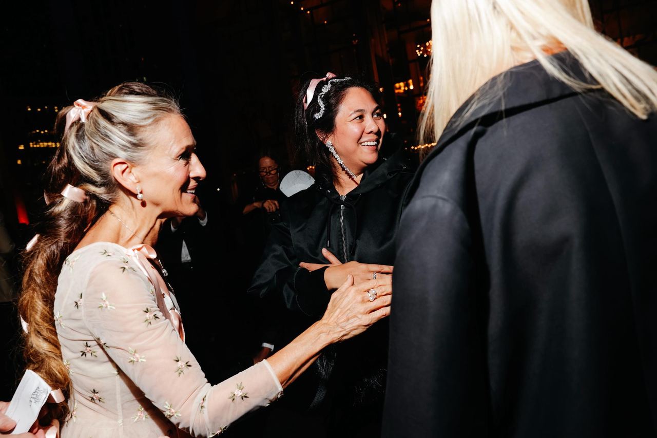Sarah Jessica Parker mingles with designer Simone Rocha, in New York City, with pink ribbons offering a subtle preview of Parker's elaborate look. | Source: Getty Images