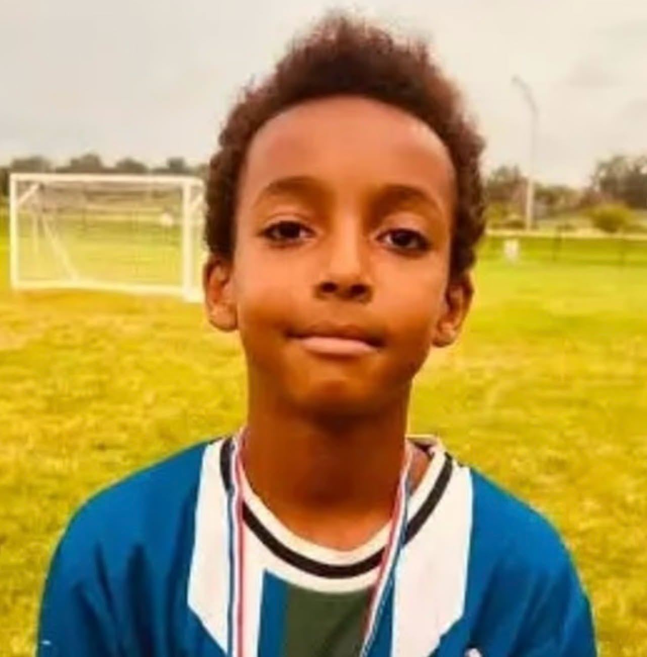 Ten-year-old Ahmed Osman poses in a blue and white sports jersey wearing a medal around his neck, standing on a grass soccer field with goalposts visible in the background. | Source: Facebook/The Robbie Harvey
