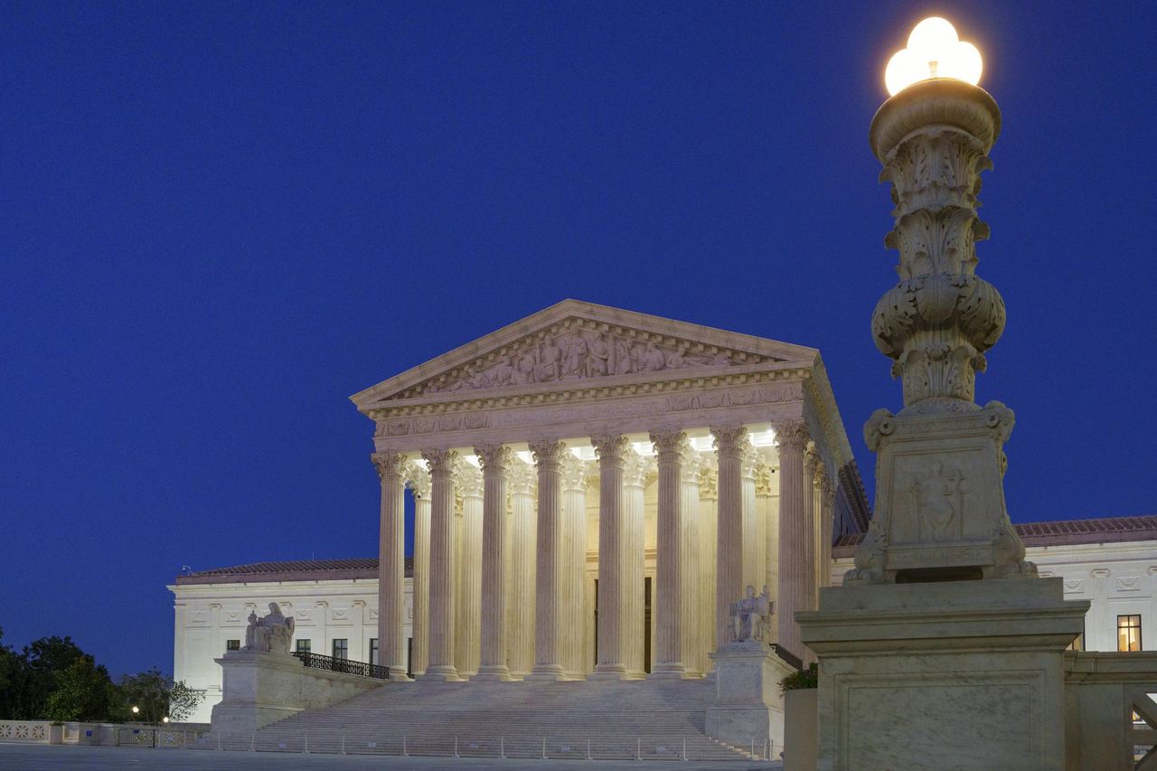 The illuminated neoclassical facade of the U.S. Supreme Court building glows against a deep blue evening sky at twilight on September 14, 2026, in Washington, D.C. Seen from the plaza steps, an ornate, glowing marble lamppost anchors the foreground, highlighting the iconic Corinthian columns and pediment sculptures of the nation's highest court. | Source: Getty Images