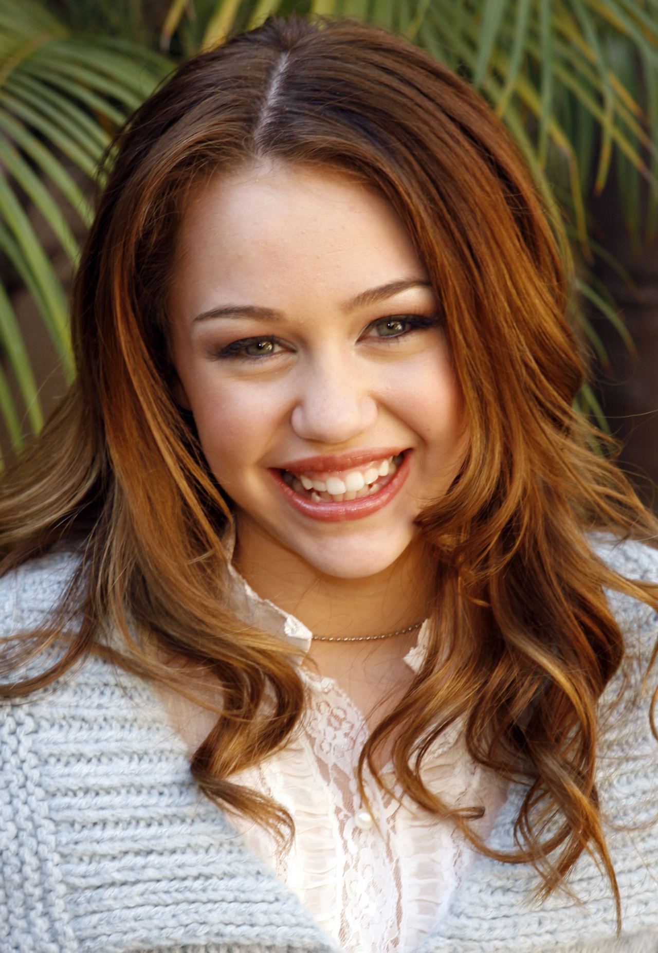 Miley Cyrus smiled for the camera with long, highlighted brown hair and a white lace-trimmed blouse, offering a glimpse of her youthful look before her transformation into a global pop star. | Source: Getty Images